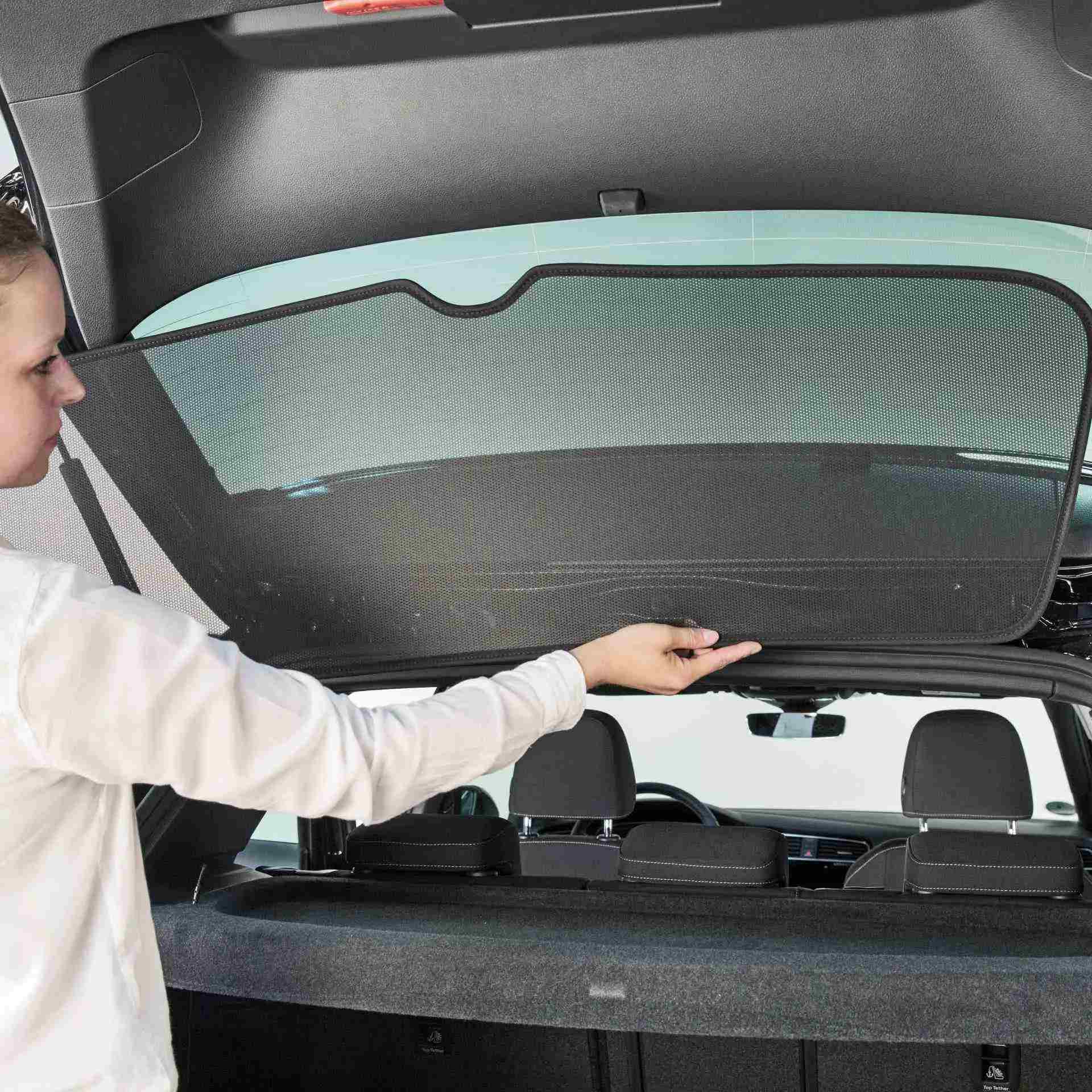 eine Frau bringt den Sonniboy an die Heckscheibe eines Autos an