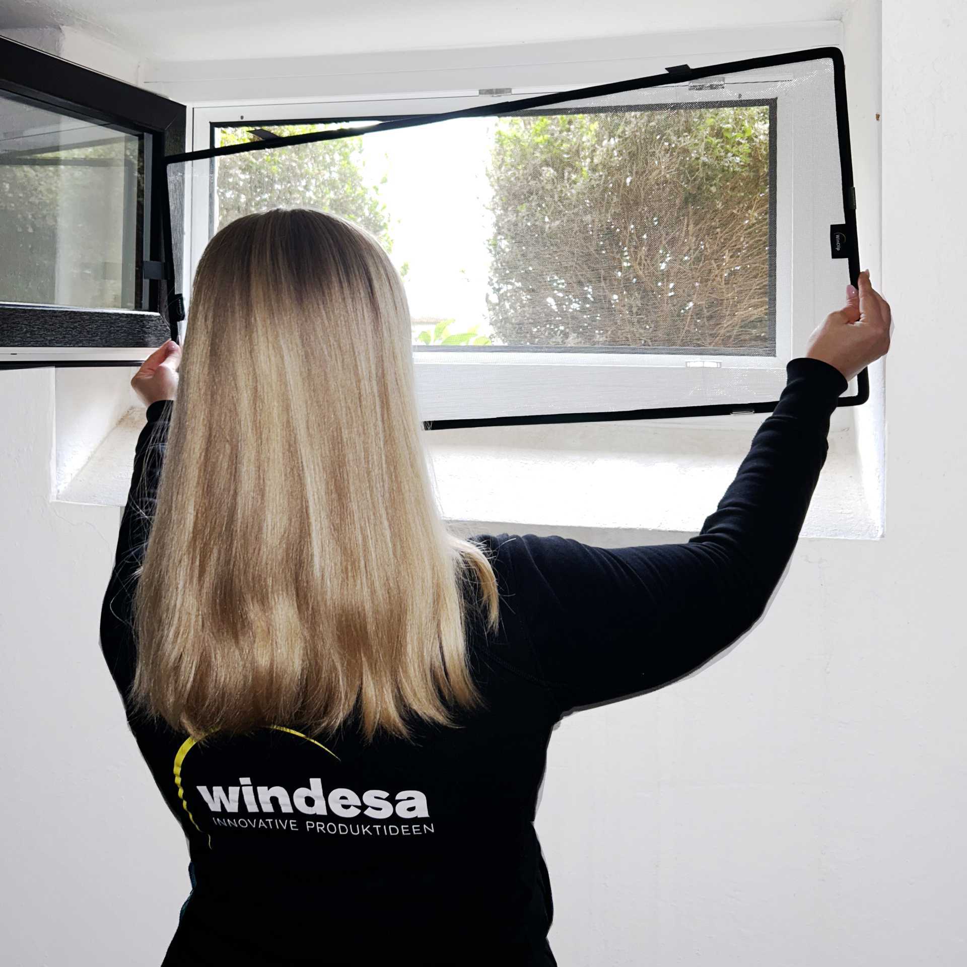 A woman installs the WinClip on a basement window