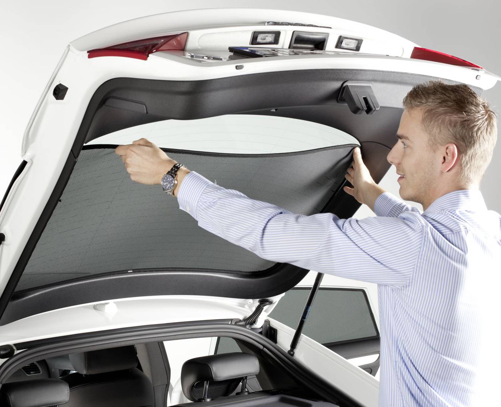 a man attaches a sun screen at the rear window of a car