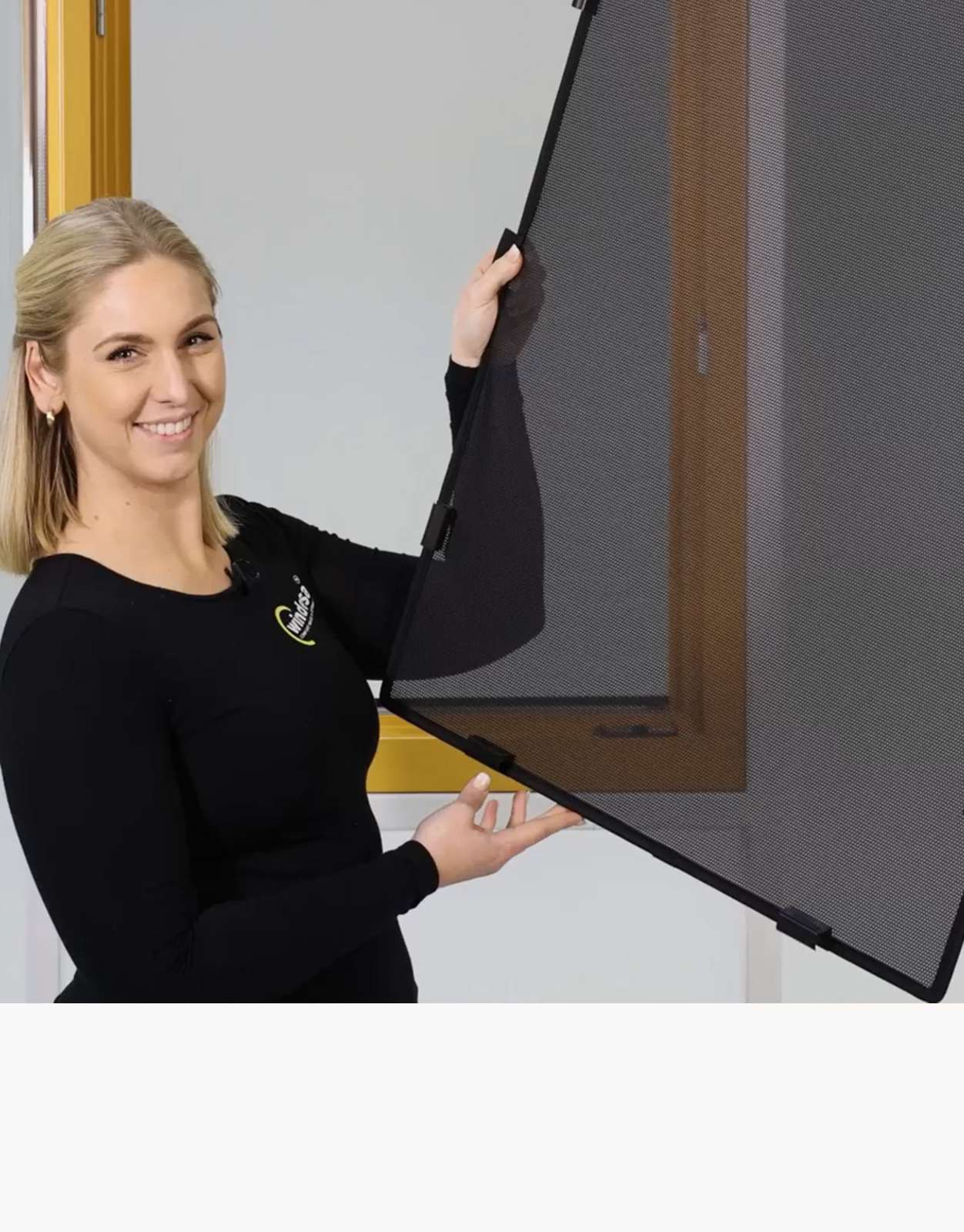 WinClip Fensterschutzsystem eine Frau hält lächelnd den WinClip vor einem Holzfenster in den Händen