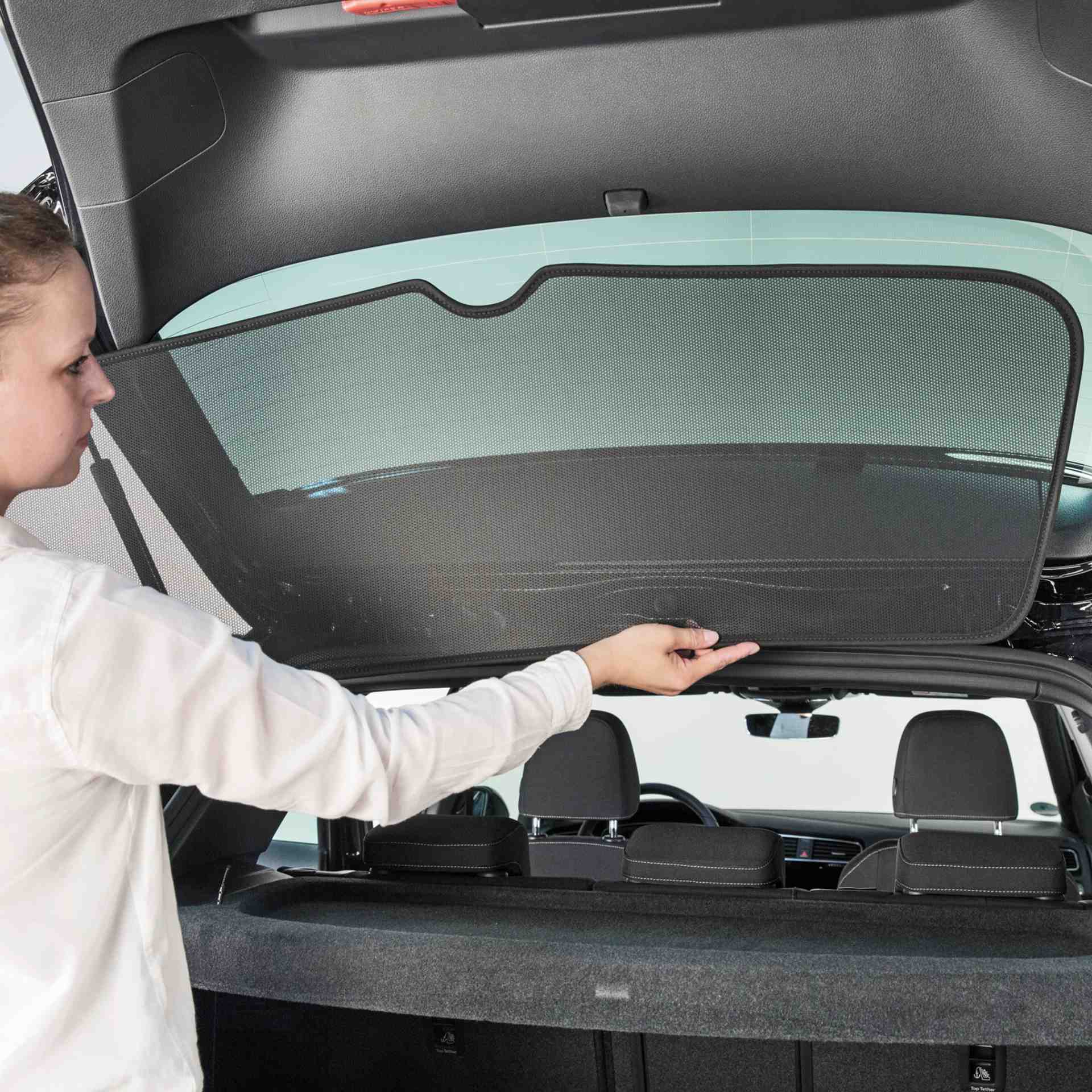 eine Frau bringt die Sonnenblende für die Heckscheibe an