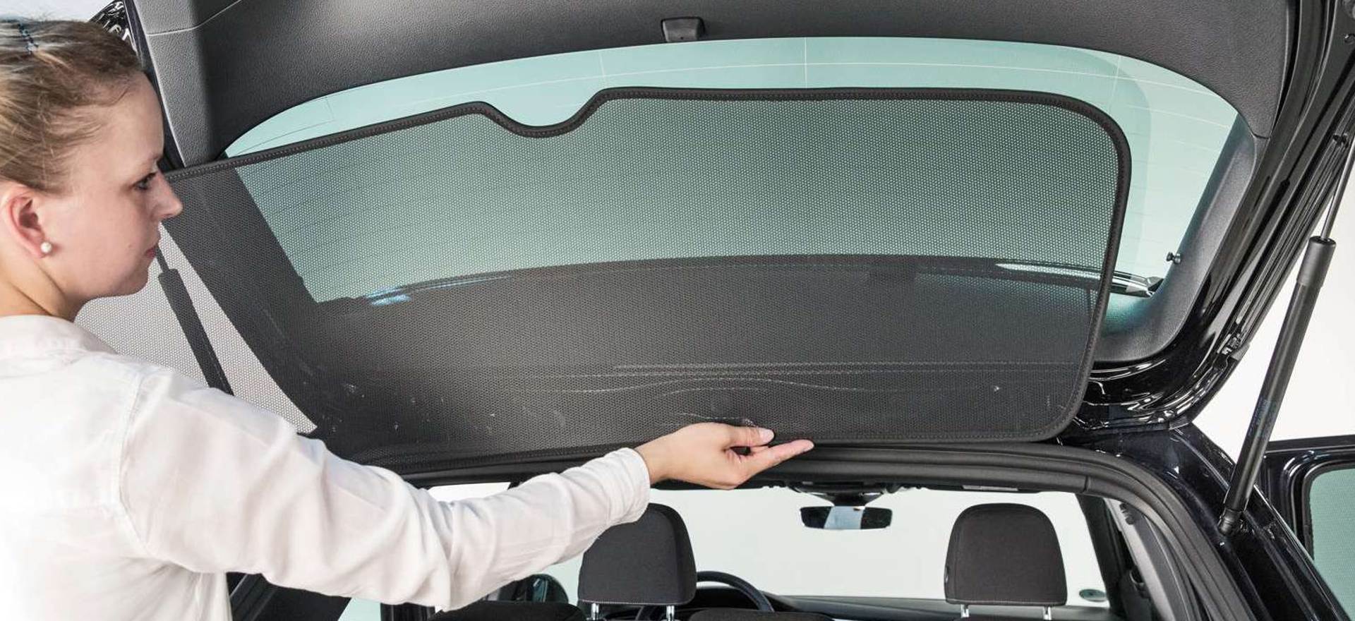 eine Frau setzt ein Sonnenschutzelement an der Heckscheibe eines Autos ein